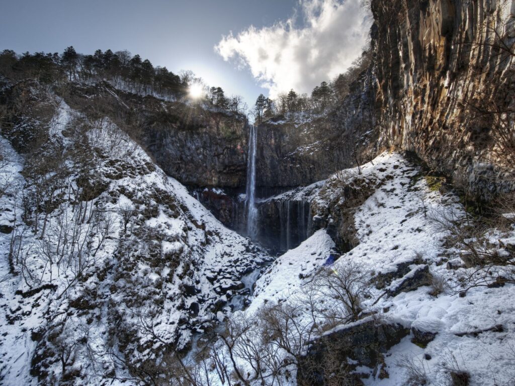 Serene morning waterfall cascading over frost-covered rocks with sunlight and mist background Wallpaper