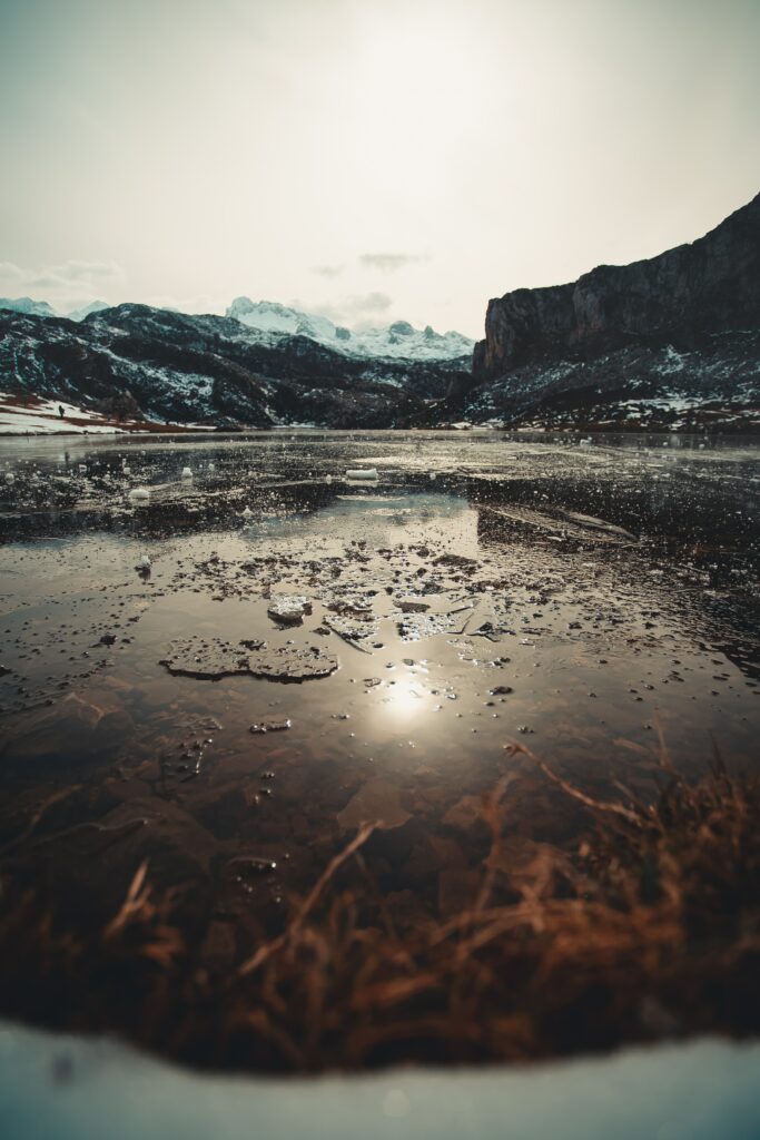 Tranquil partially frozen lake reflecting cloudy sky framed by majestic mountains and snowy valley Wallpaper