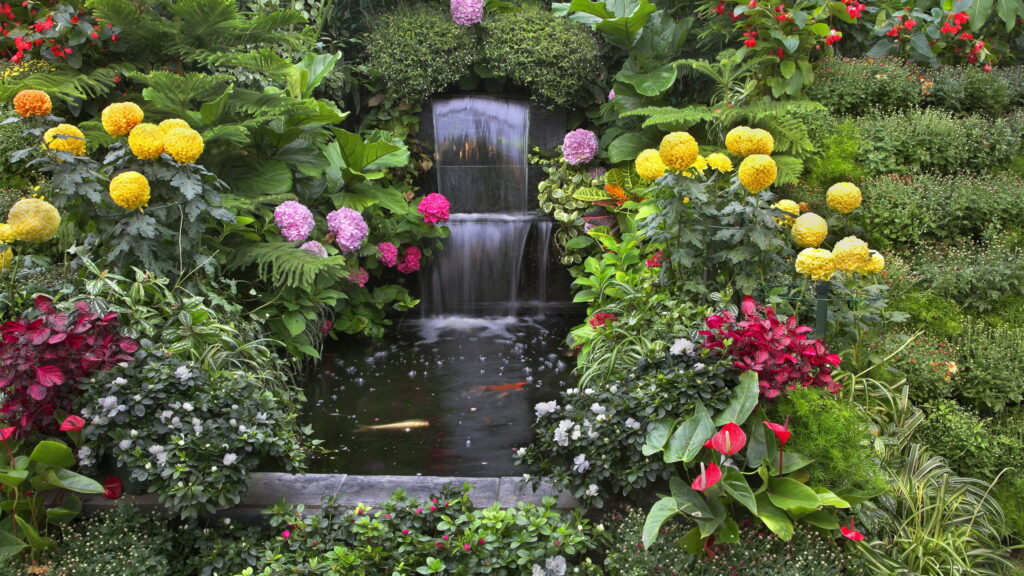 Tranquil Oasis: A QHD Wallpaper of a Lush Garden with Florals and a Serene Small Waterfall