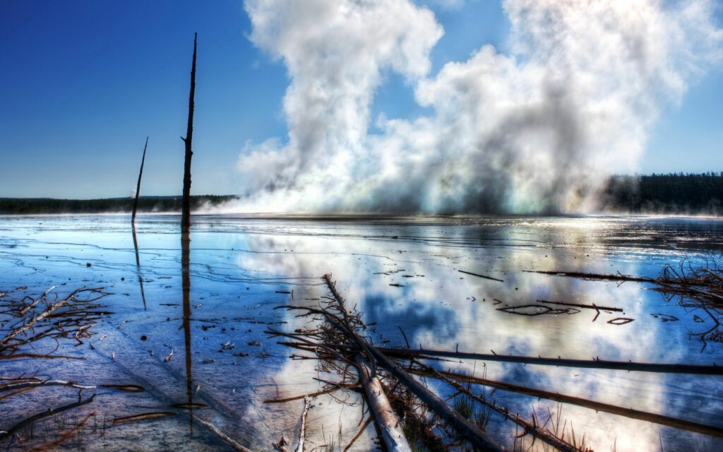 Reflective water with bare trees and rising steam under vivid blue sky geothermal landscape wallpaper