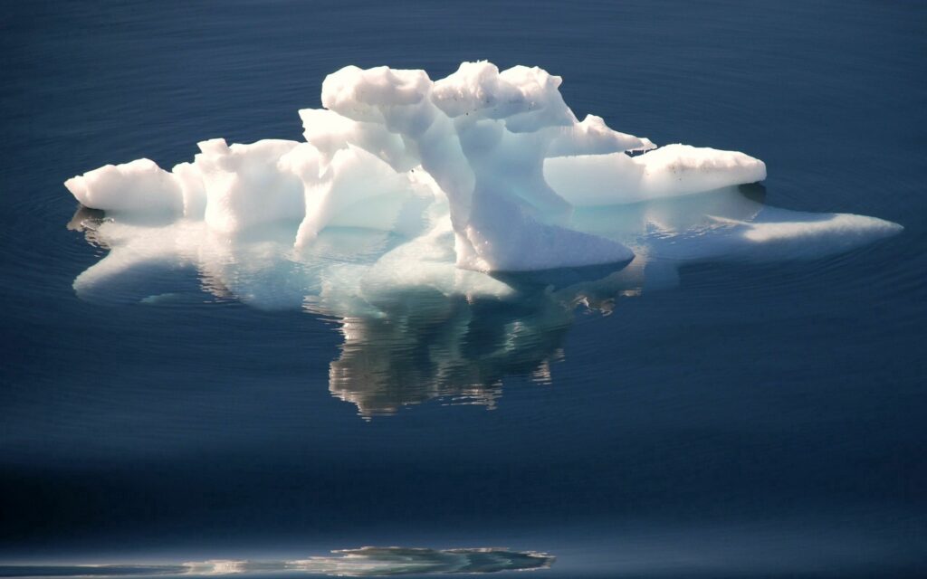 Solitary glacier fragment floating on calm deep blue water reflecting serene natural beauty wallpaper