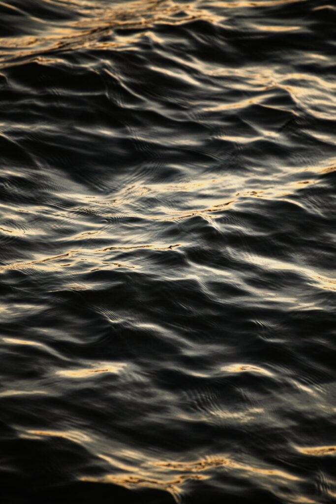 Close-up of water ripples with golden light reflections creating serene natural wave patterns Wallpaper