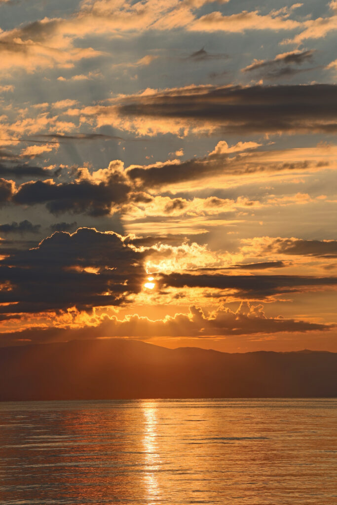 Breathtaking golden sunset over calm water with dramatic clouds and shimmering reflection wallpaper