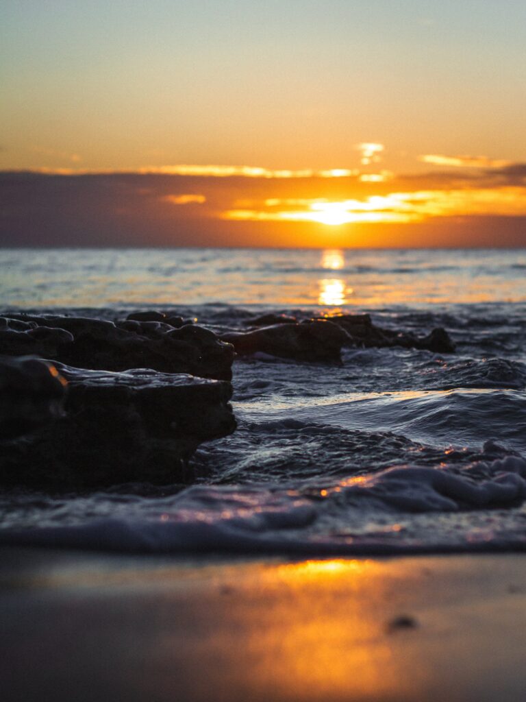 Serene sunset over sea with golden light on waves and wet stones coastal wallpaper background