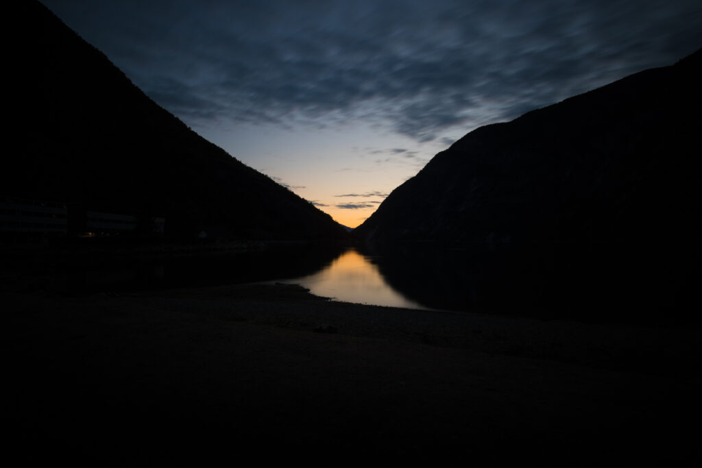Serene sunset over tranquil lake with golden glow dark hill silhouettes and vibrant sky reflections Wallpaper