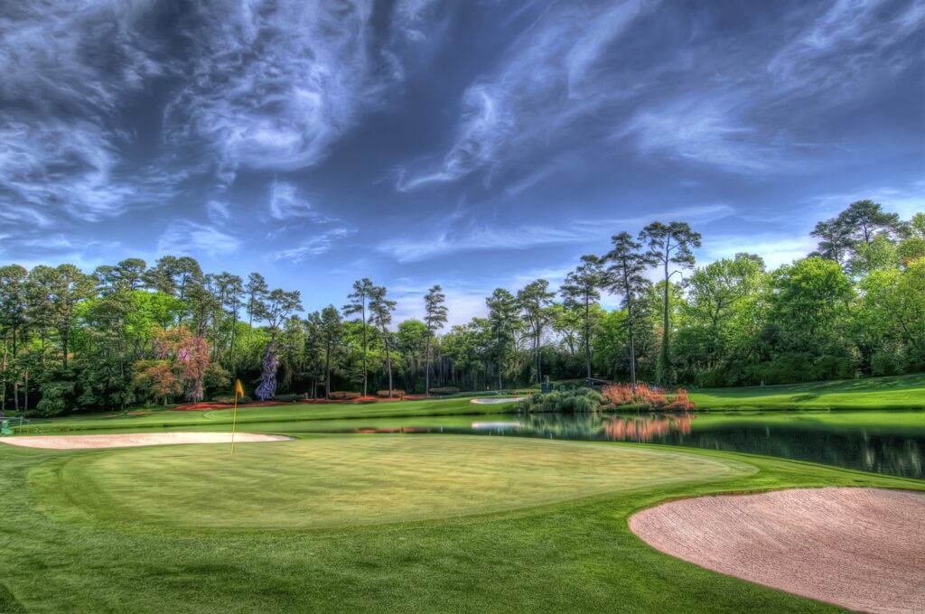 Lush golf course with tall trees calm water and dramatic cloudy sky vibrant HD wallpaper background