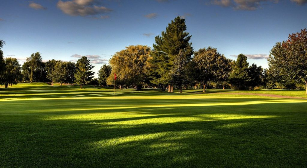 Serene golf course wallpaper with green fairway red flag and long shadows under blue sky