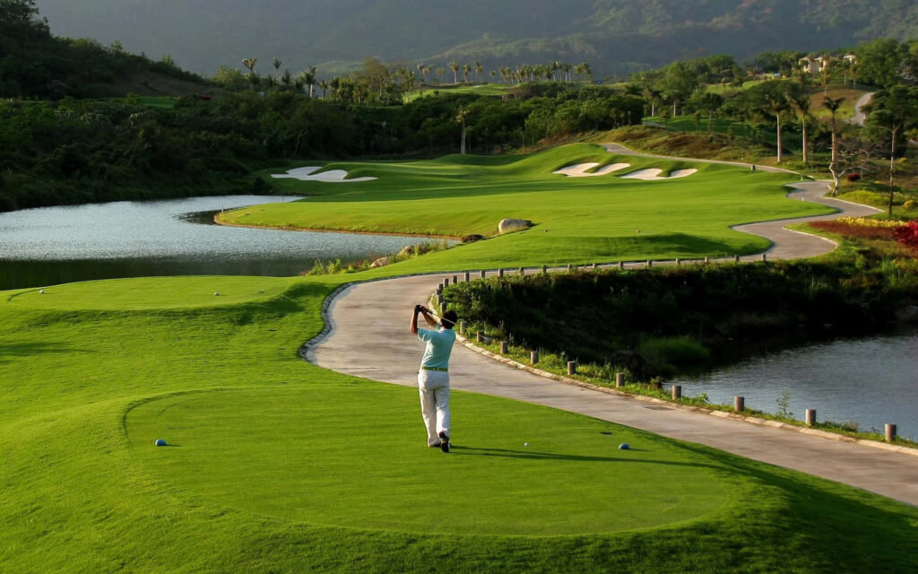 Man Swinging on Lush Golf Course with Hills and Water Hazard Wallpaper