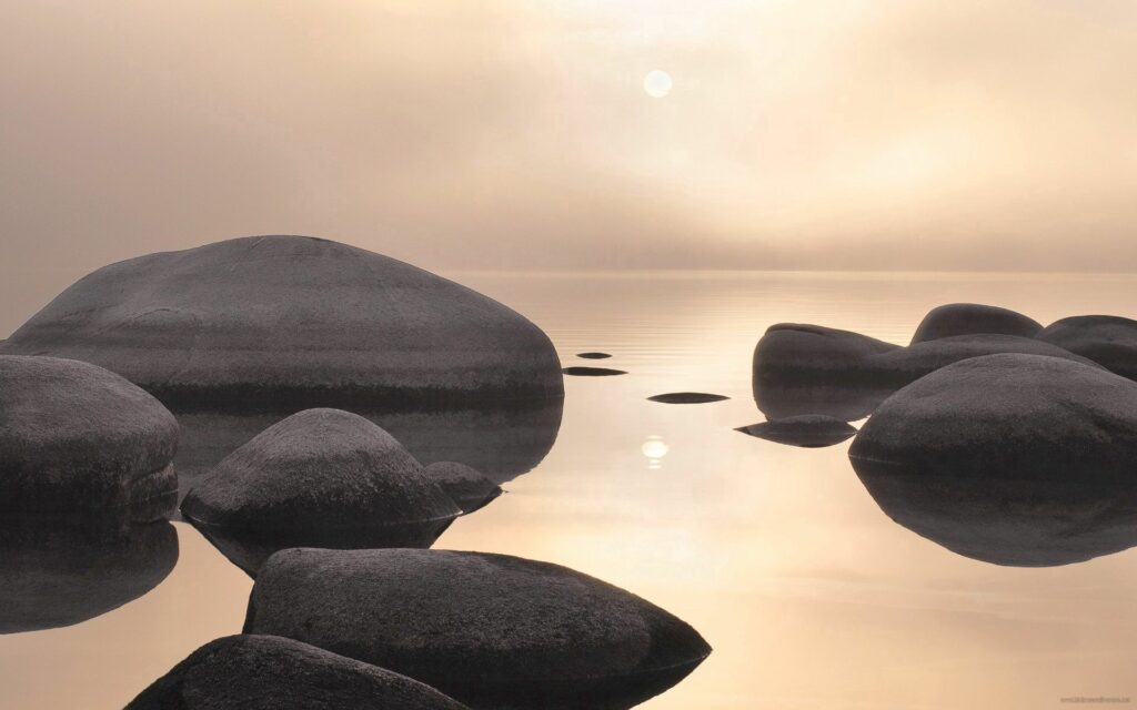 Calm gray stones on water reflecting soft misty light in a peaceful minimalist wallpaper background