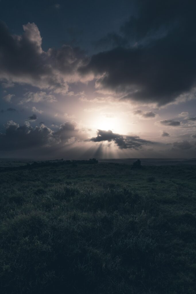 Serene green field with dramatic sunlight piercing cloudy sky peaceful nature wallpaper background