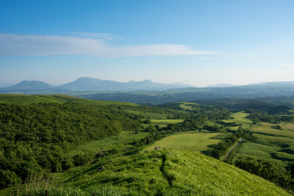Breathtaking landscape of rolling green hills lush vegetation and mountains under clear blue sky Wallpaper