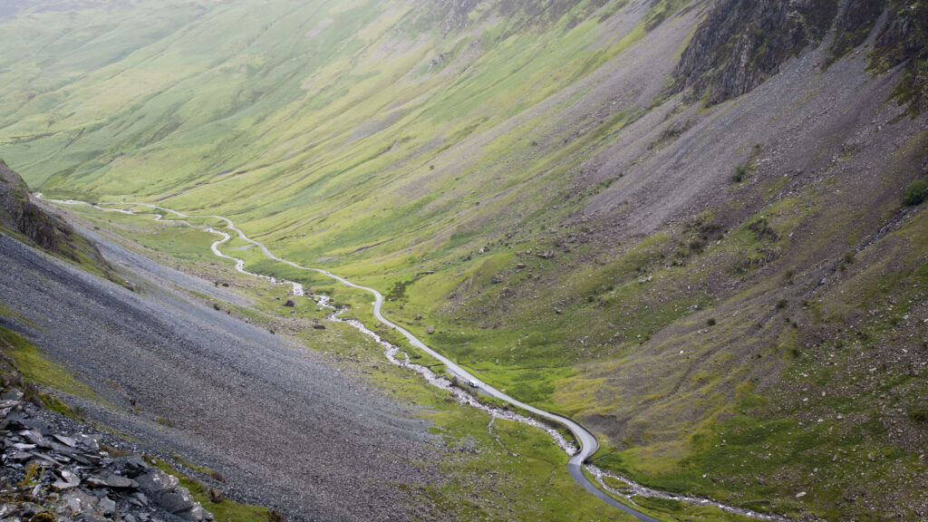 Serene landscape wallpaper with winding stream in lush green valley and rocky slopes background