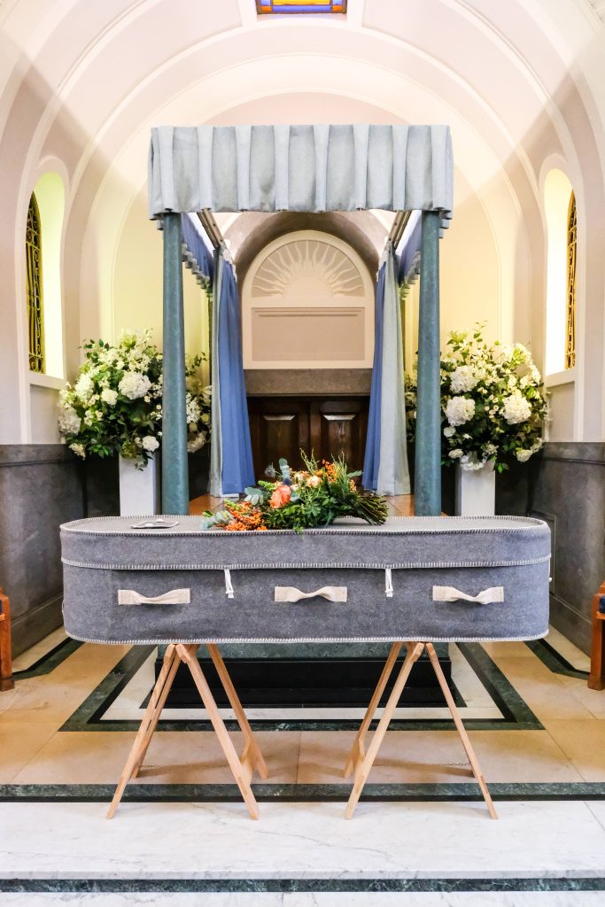 Grey biodegradable felt coffin with floral bouquet in serene chapel funeral setting wallpaper