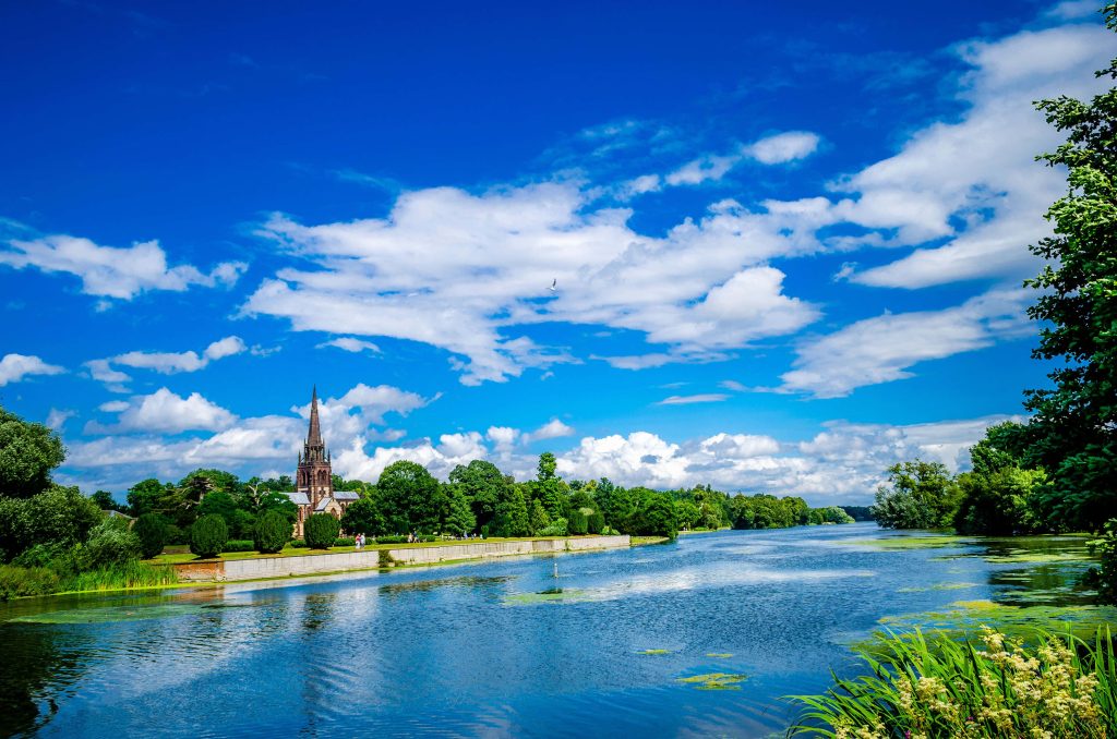 Holy Trinity Church Stratford spire above River Avon lush trees blue sky scenic landscape view Wallpaper