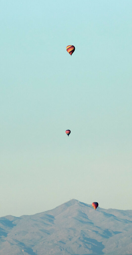 Three colorful hot air balloons floating over rugged mountains under a clear blue sky wallpaper