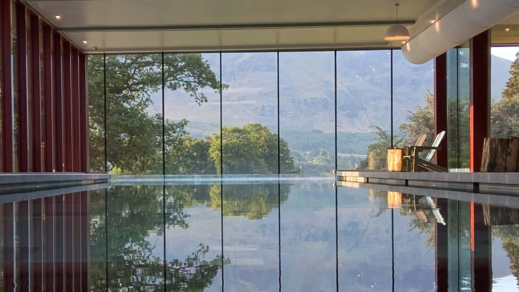 Indoor pool with floor-to-ceiling windows overlooking lush greenery and mountains calming water reflections Wallpaper