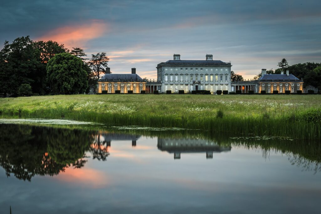 Elegant Irish manor with lush greenery and sunset reflected in calm pond serene wallpaper background