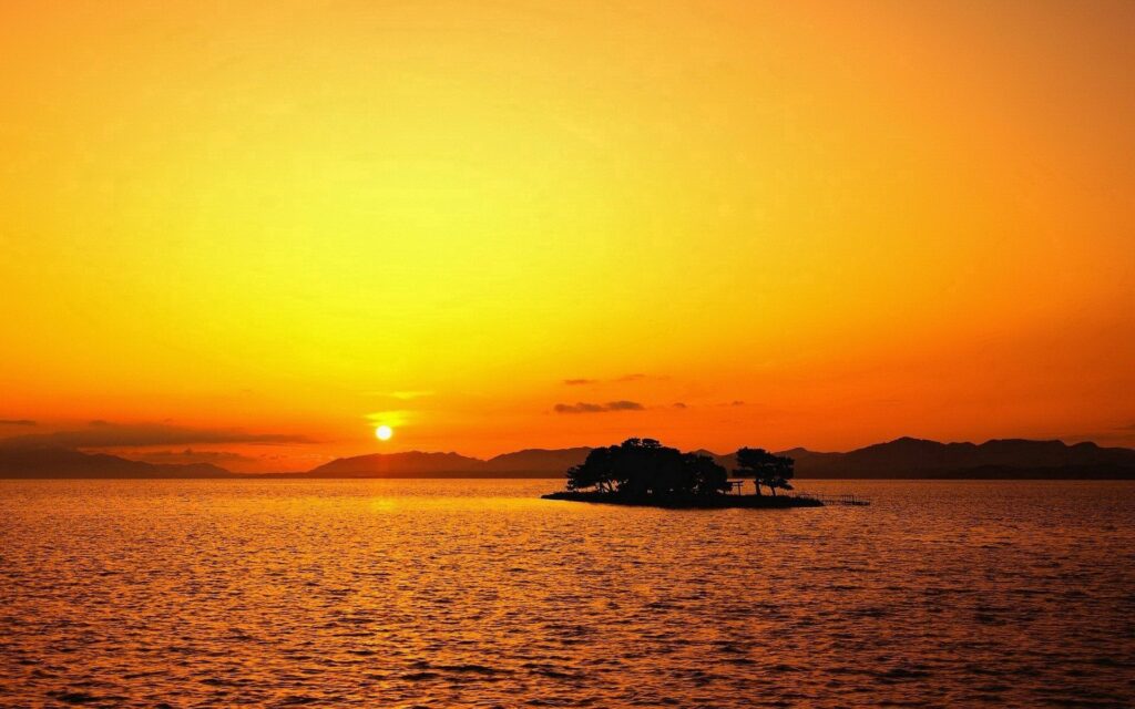 Sunset island silhouette wallpaper with vibrant orange sky gentle sea ripples and tree outlines