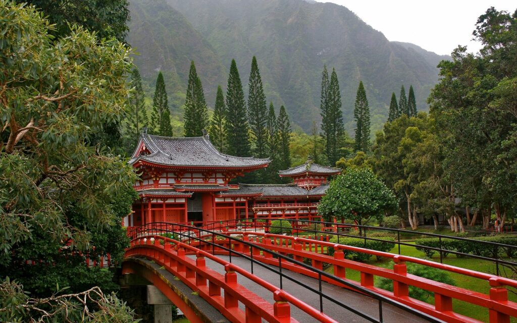 Serene Japanese red bridge with traditional architecture lush trees and misty mountains wallpaper