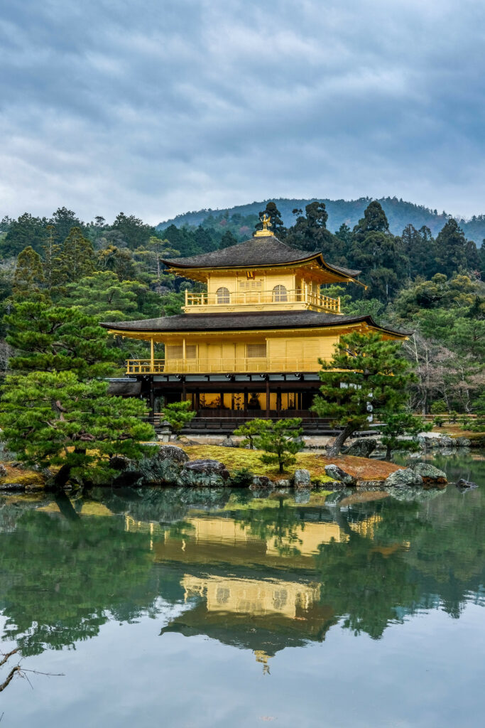 Japanese temple with golden pagoda reflected in calm water surrounded by lush greenery wallpaper