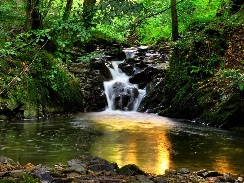 Serene Klein-Pyokhlarn waterfall over mossy rocks with lush greenery and sunlight reflection wallpaper