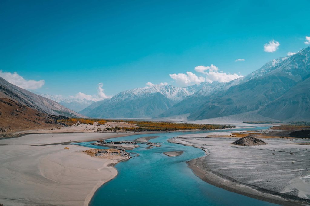 Turquoise river flowing through Ladakh sandy valley with snow-capped mountains blue sky background Wallpaper