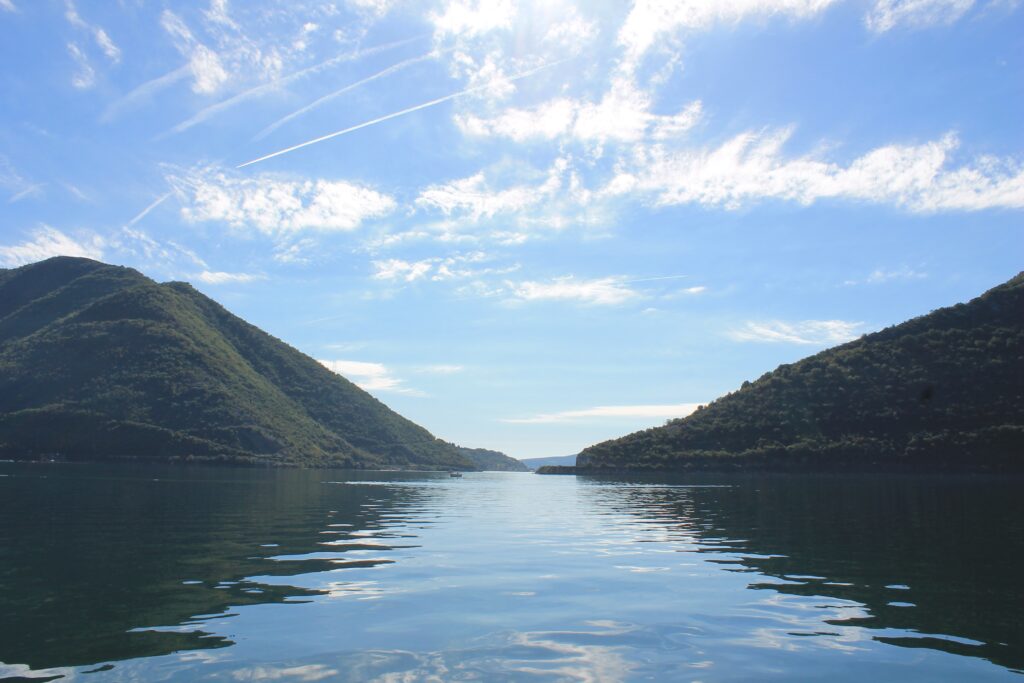 Tranquil lake between green mountains under blue sky with clouds and contrail reflection wallpaper