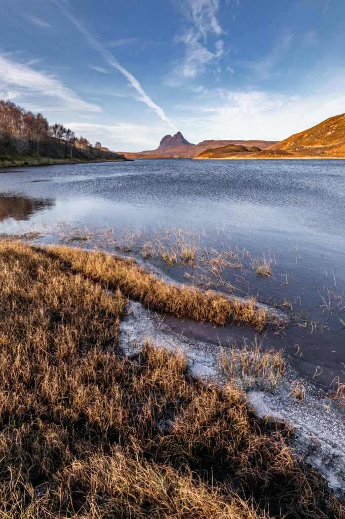 Serene lake with grassy shore and rugged mountains under clear blue sky natural landscape wallpaper