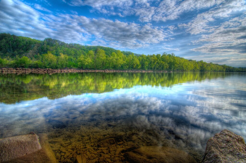 Serene lake with lush green forest and dramatic sky reflecting in calm water landscape wallpaper