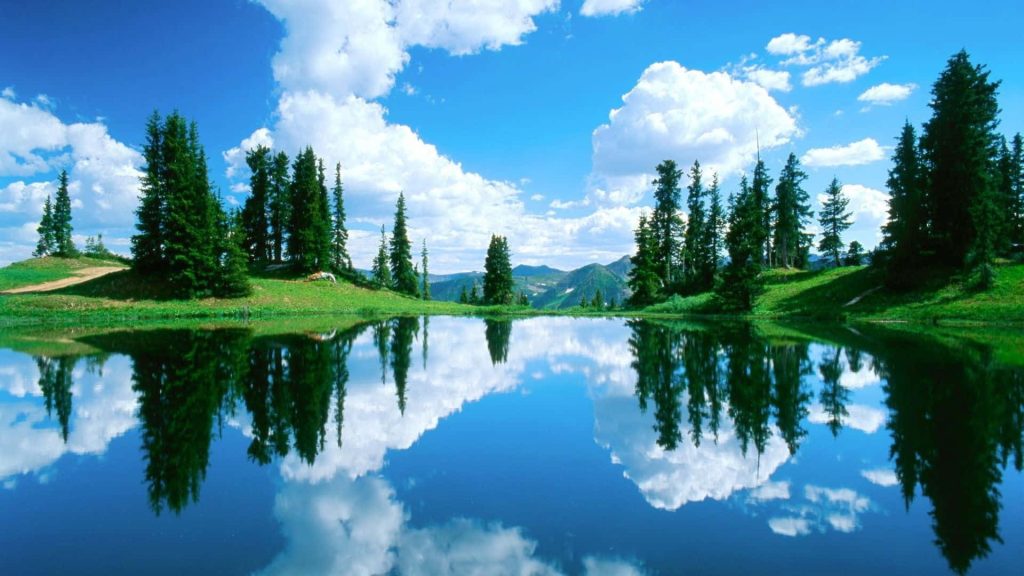 Serene lake reflecting green trees and mountains under a blue sky with white clouds desktop wallpaper