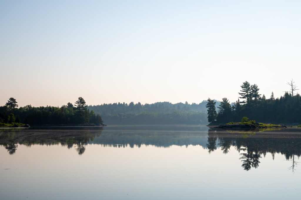 Serene lake landscape with clear reflections trees small island pale blue sky peaceful wilderness wallpaper