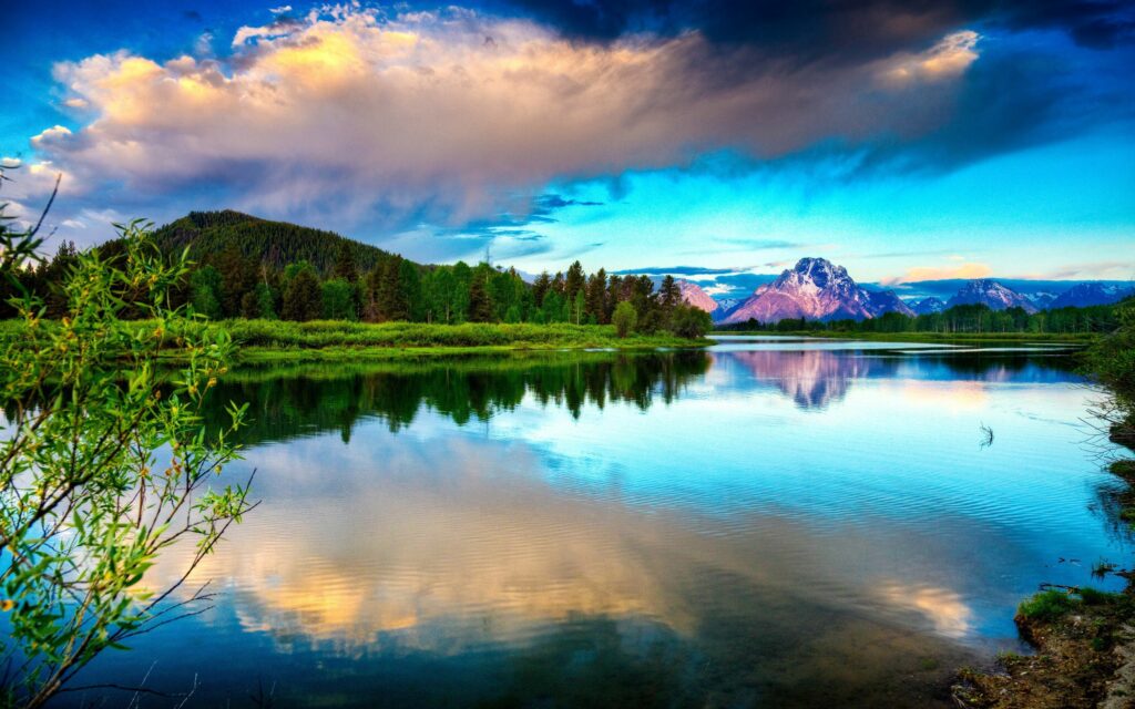 Serene lake reflecting dramatic clouds lush green mountains and bright blue sky vibrant wallpaper