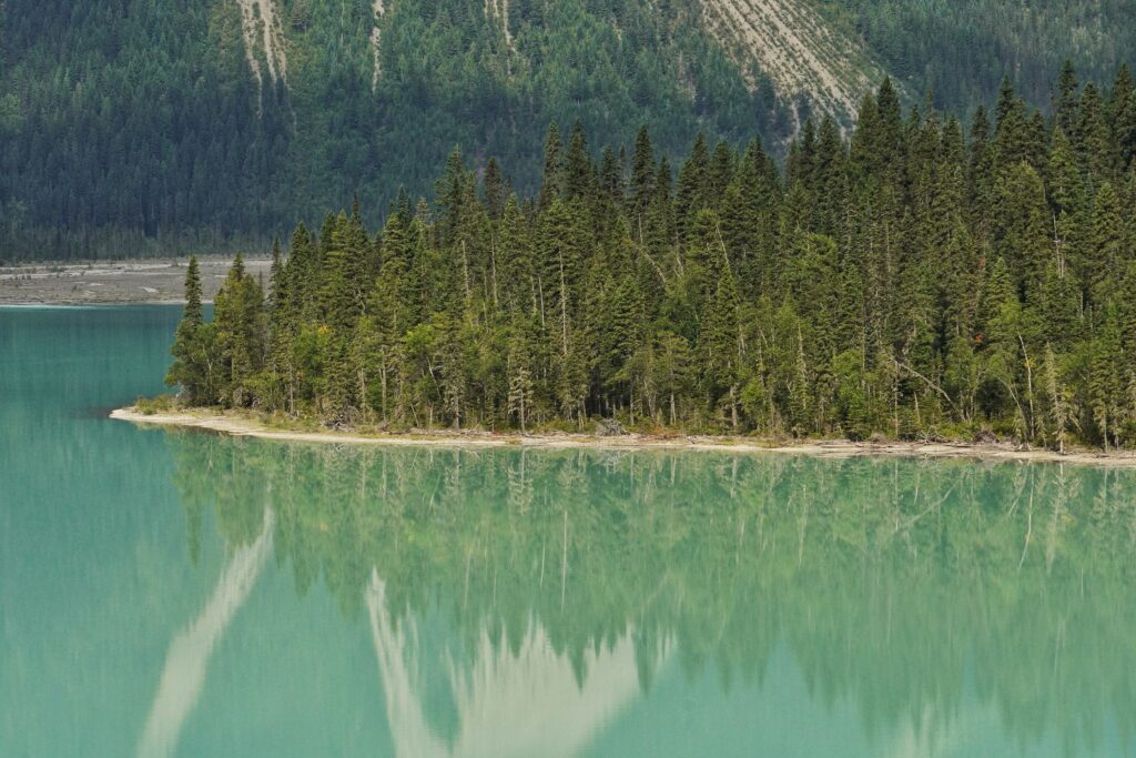 Serene turquoise lake reflecting evergreen forest and small island with mountain backdrop wallpaper