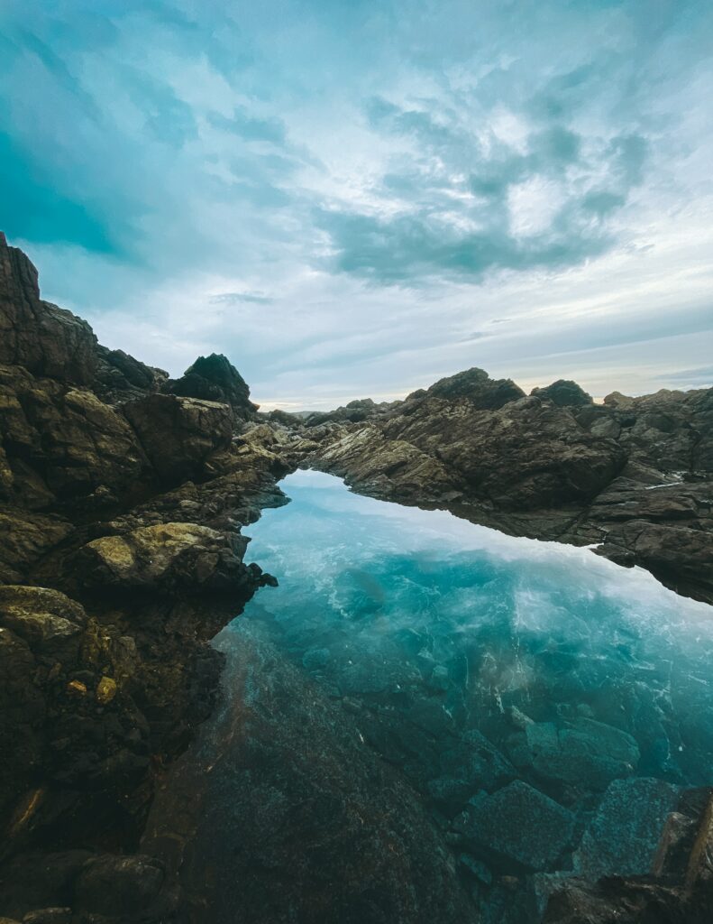 Serene lake with rugged rocks reflecting vibrant sky and dramatic clouds in natural landscape Wallpaper
