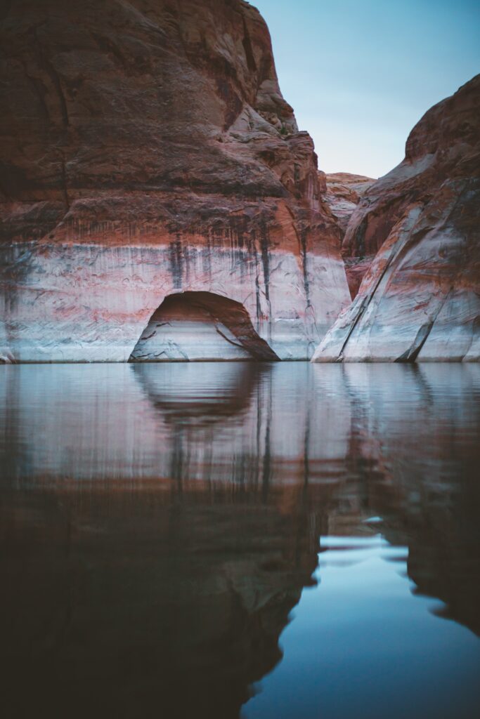Serene lake with towering rock formations and reflective cave entrance nature landscape wallpaper