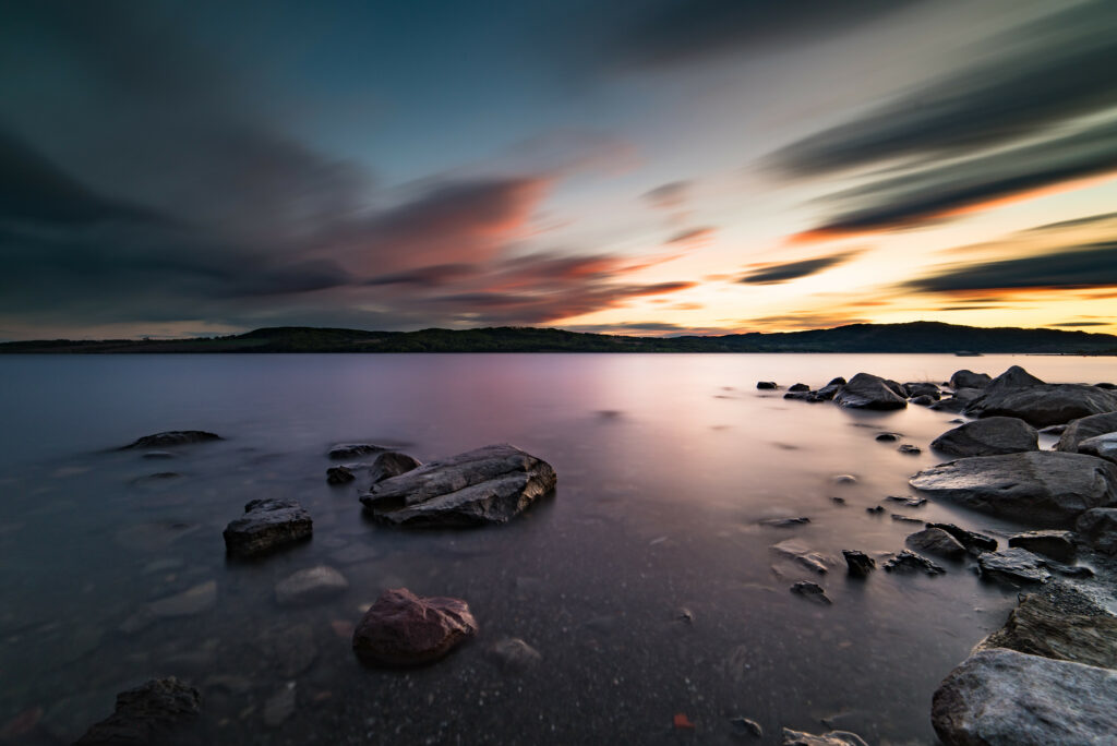 Serene lake at sunset with smooth stones rugged rocks vivid orange pink blue sky reflection wallpaper