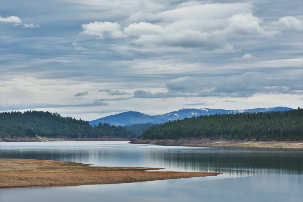 Tranquil lake reflecting green hills and dense forest under overcast sky serene nature wallpaper