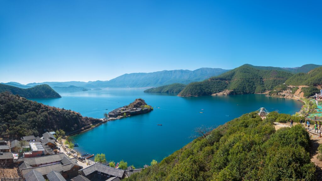 Top view of serene lake with island surrounded by green mountains under clear blue sky wallpaper