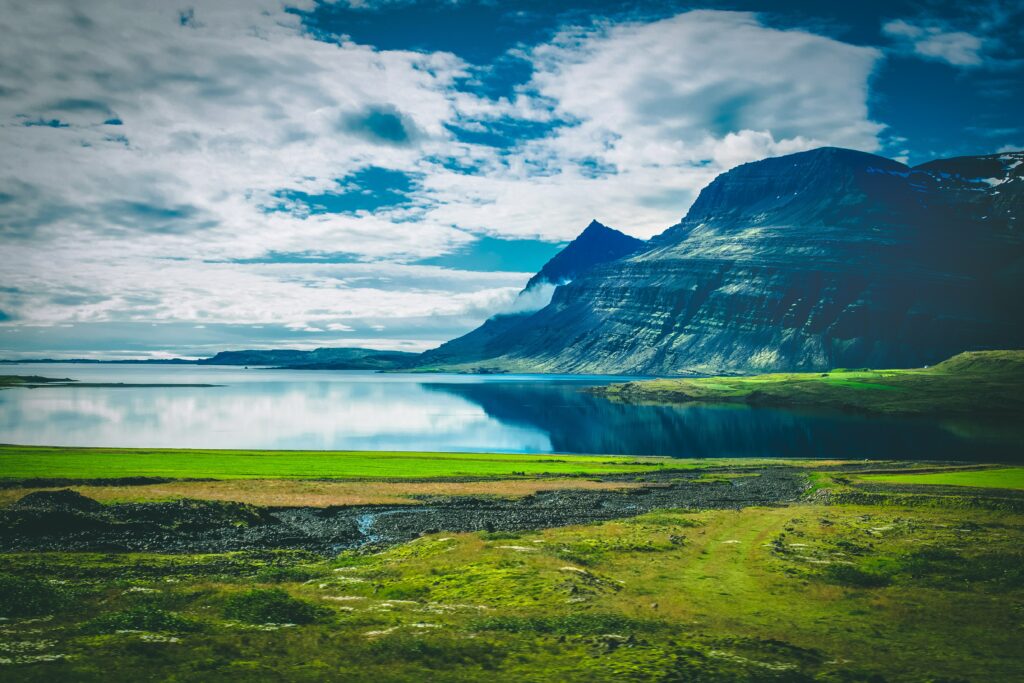 Serene lake reflecting rugged mountains lush meadows and cloudy sky with isolated island landscape Wallpaper