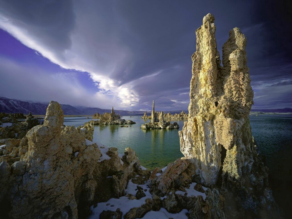 Serene lake with towering stone formations under a cloudy sky reflecting rugged natural landscape wallpaper