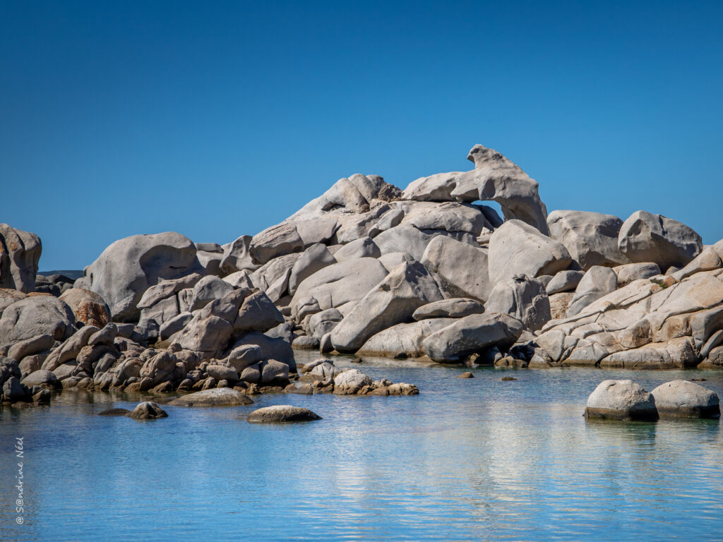 Serene lake with smooth granite rocks reflecting clear blue sky vibrant nature wallpaper background