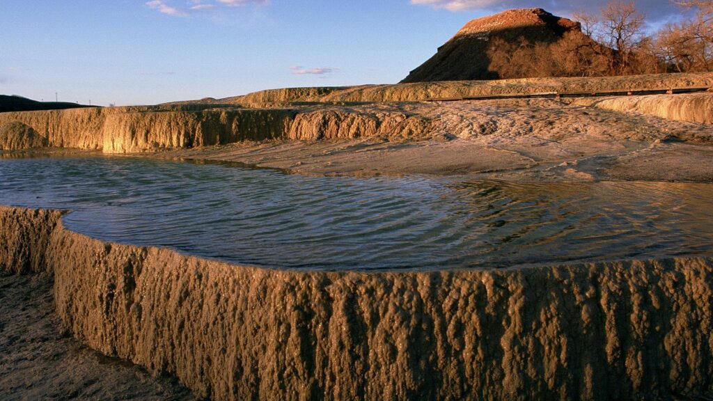 Serene lake with textured rocks and clear rippling water in earthy tones of brown and blue wallpaper
