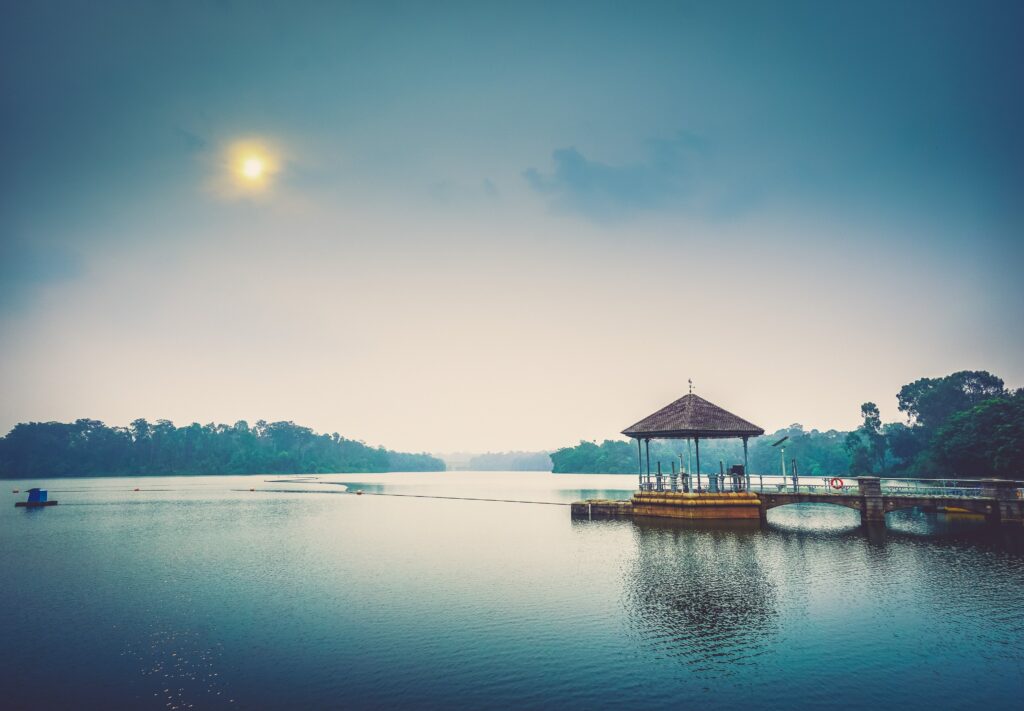 Serene lakeside gazebo over calm water with soft sunlight reflecting on peaceful blue lake background Wallpaper