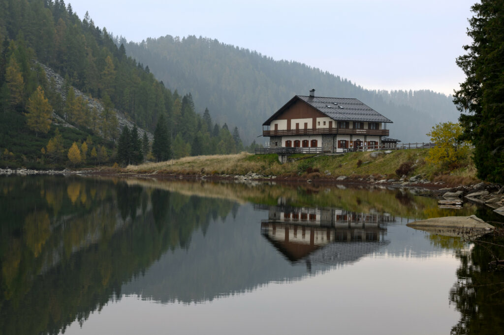 Serene lake house with forest and misty hills reflected in calm water peaceful nature scene wallpaper