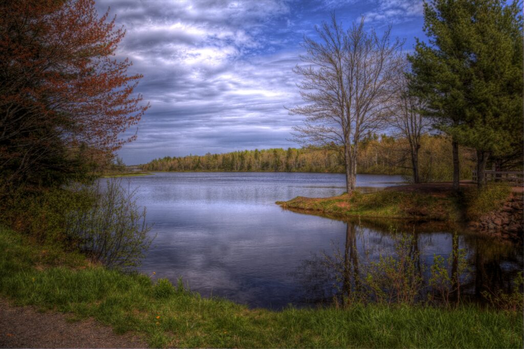 HDR lakeside landscape with calm reflections vibrant green trees and dramatic cloudy sky wallpaper