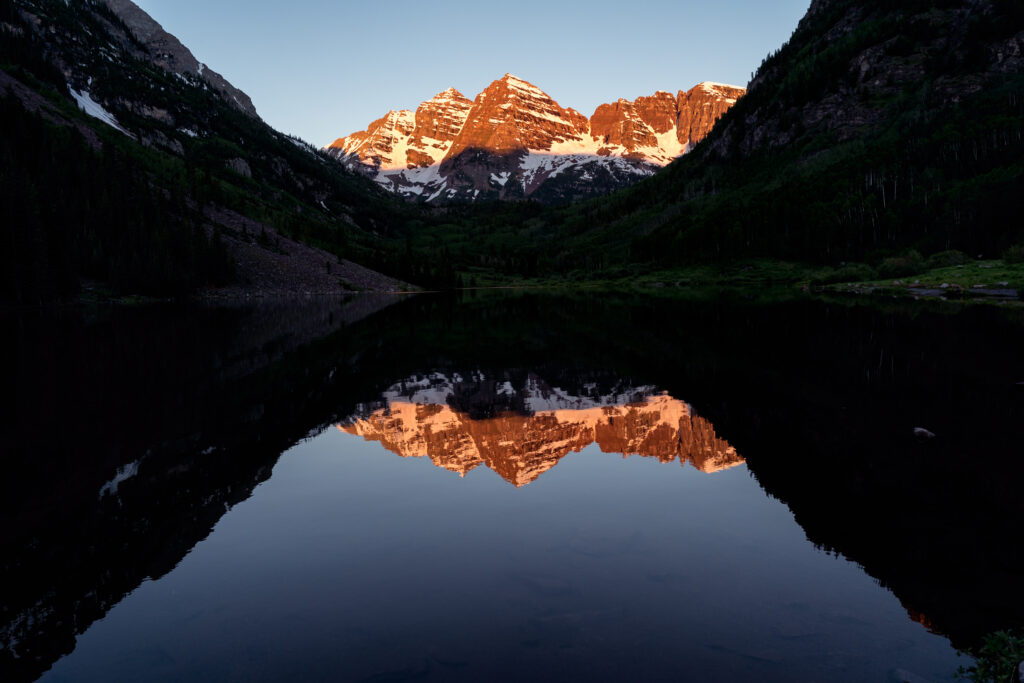 Serene lake at dusk reflecting rugged golden mountains with lush greenery and shadows wallpaper