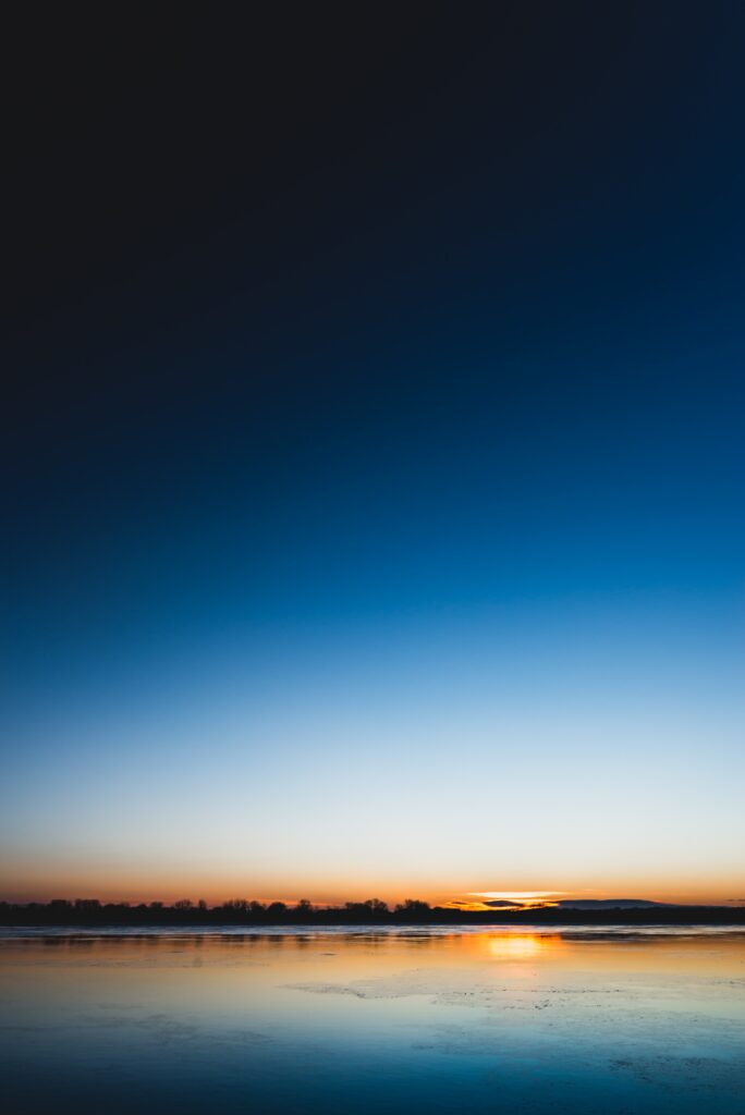 Serene lakeside sunset wallpaper with glowing horizon and calm water reflecting twilight tones