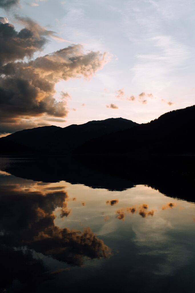 Serene lakeside sunset with golden clouds reflecting on calm water and silhouetted trees Wallpaper