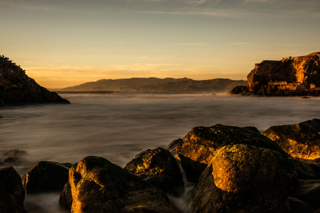 Sunset lakeside wallpaper with calm reflective water rugged rocks and distant hills serene landscape