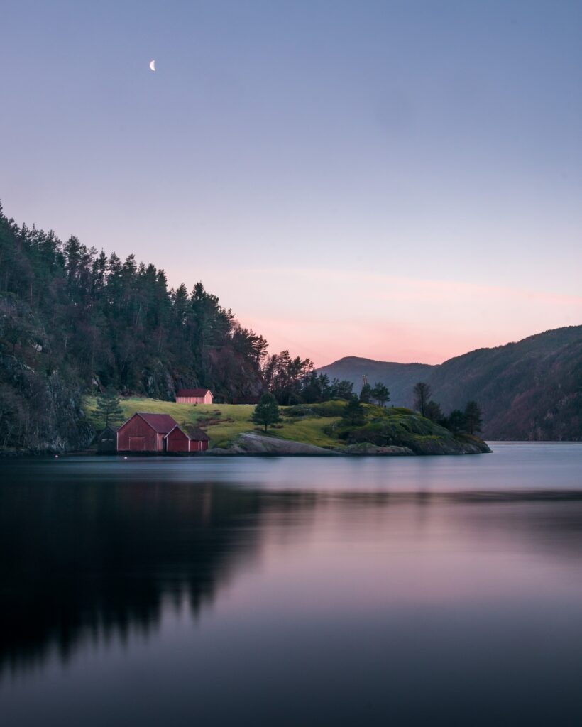 Serene lakeside with quaint house and red barn at dusk reflecting on calm water peaceful nature Wallpaper